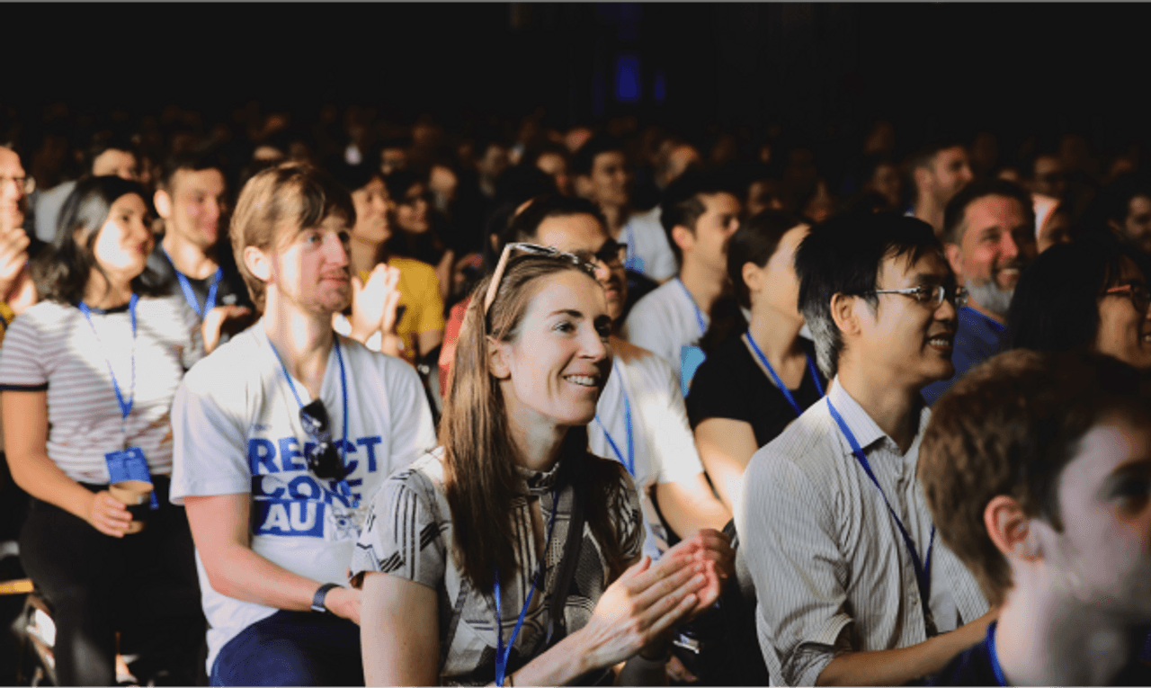 Photo of smiling attendees at ReactConf AU watching one of the talks