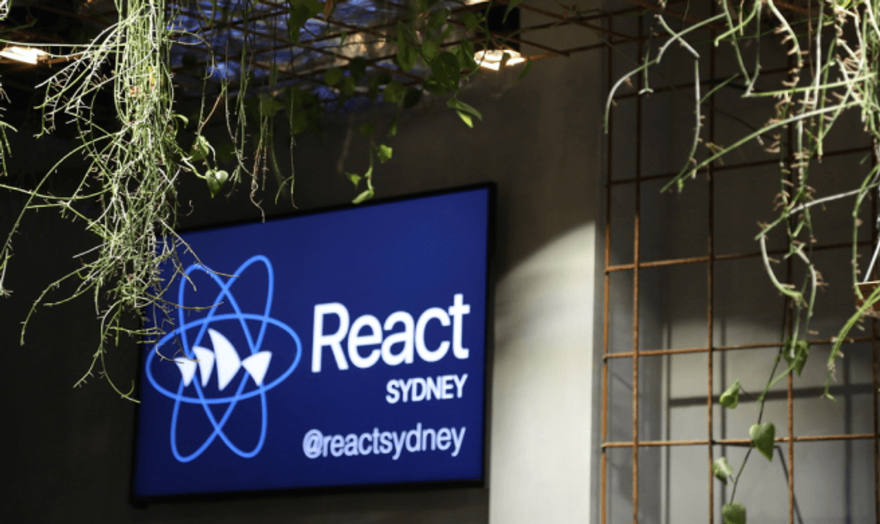 Photo of a wall mounted screen at a React Sydney event - displaying the React Sydney logo.